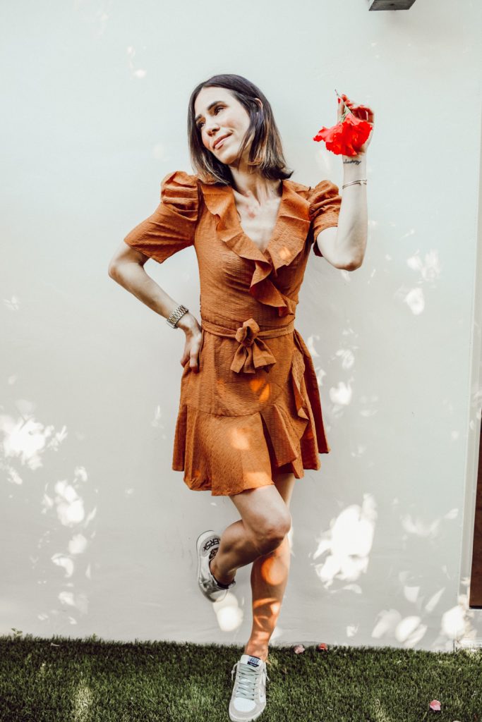 Blogger Sportsanista sharing ruffle wrap mini dress and golden goose sneakers